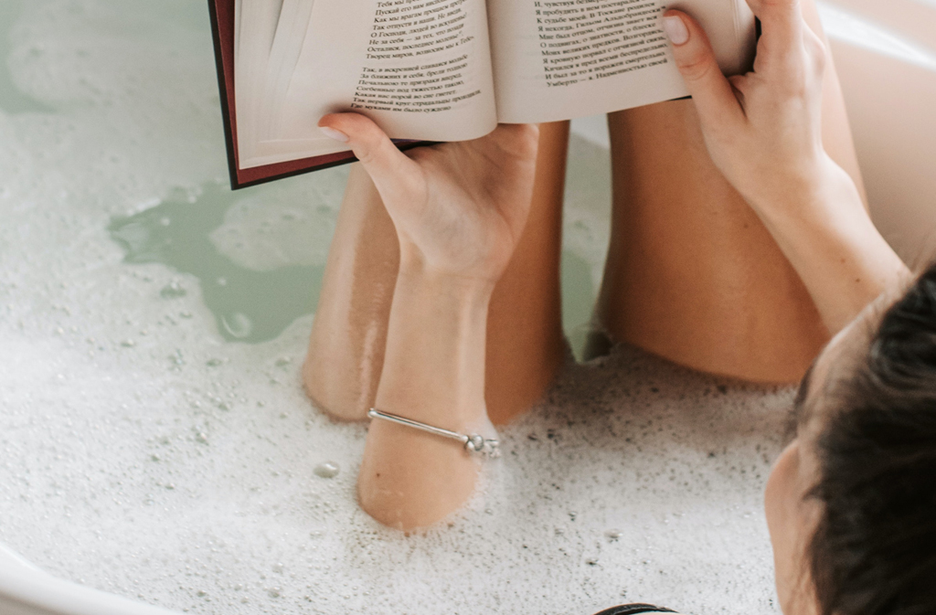 Kobieta w kąpieli czytająca książkę ze srebrną biżuterią - bransoletką na ręce. 