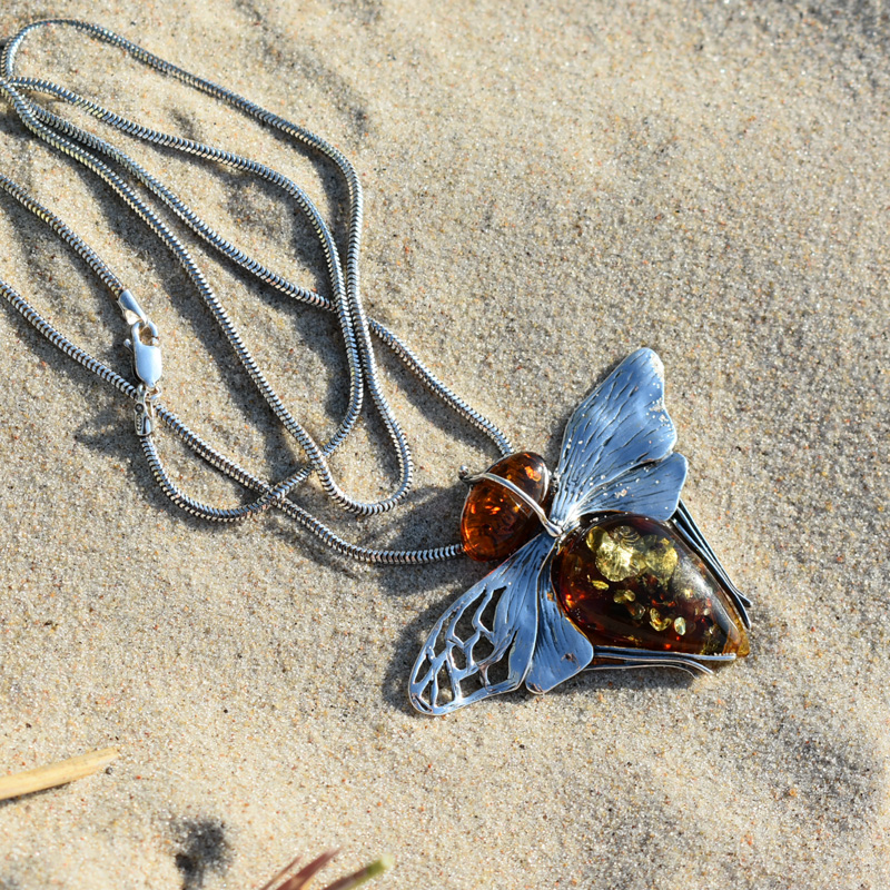 Srebrna zawieszka duża mucha z bursztynem leżąca na piasku.