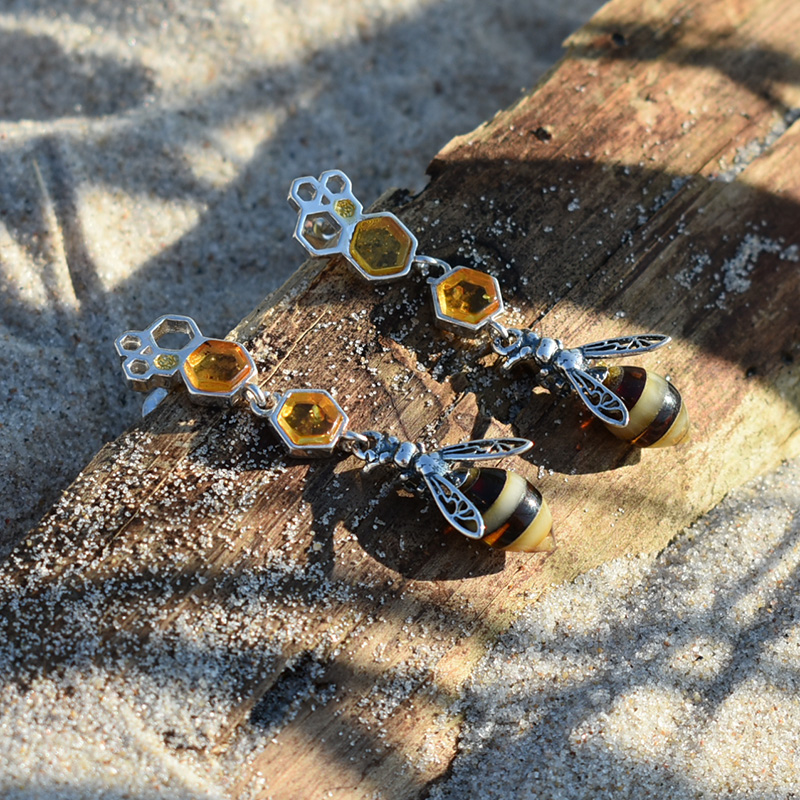 Kolczyki pszczoły wiszące przedstawione na plaży na kawałku drewna.