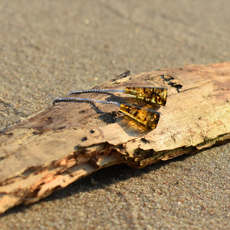 Kolczyki wiszące z zielonym bursztynem leżące na plaży na kawałku drewna.
