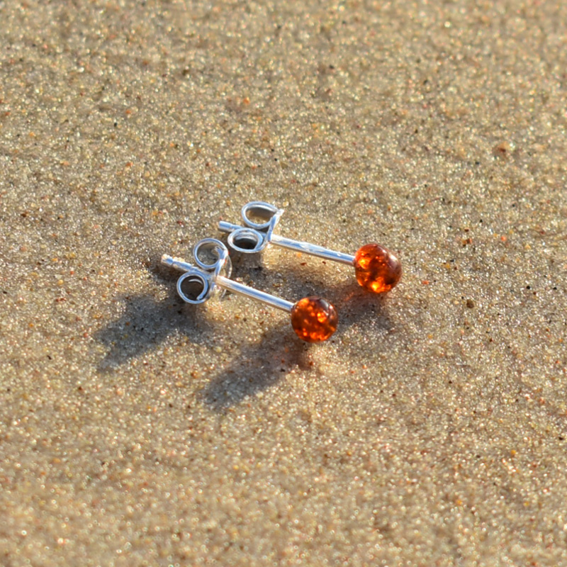 Kolczyki kulki z bursztynem leżące na plaży.