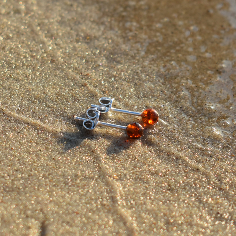 kolczyki kulki z bursztynem leżące na plaży.