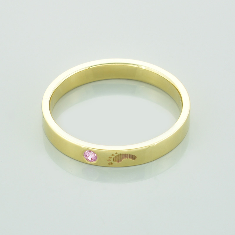 Złoty pierścionek stópka z różową cyrkonią leżący.