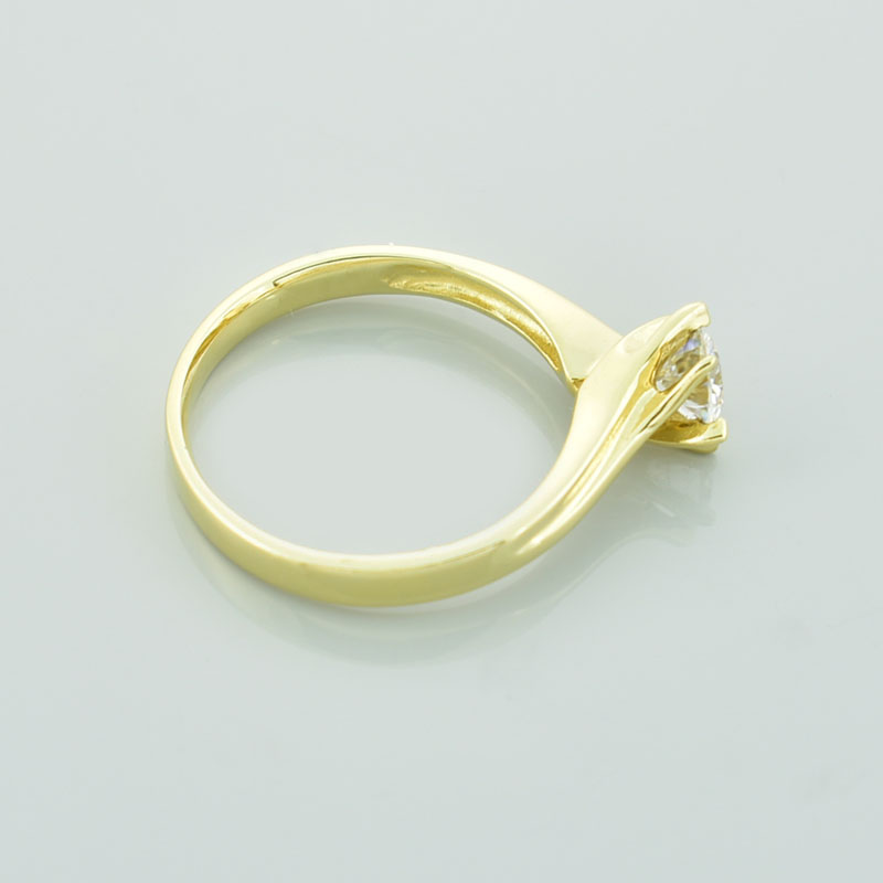 Złoty pierścionek z moissanitem leżący na prawym boku.