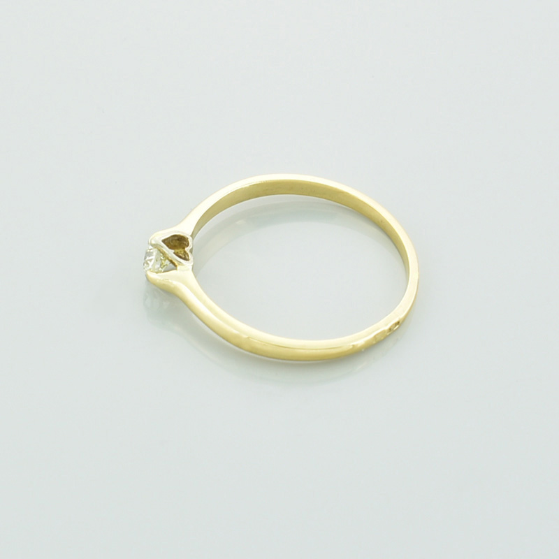 Złoty pierścionek z brylantem serce leżący na lewym boku.