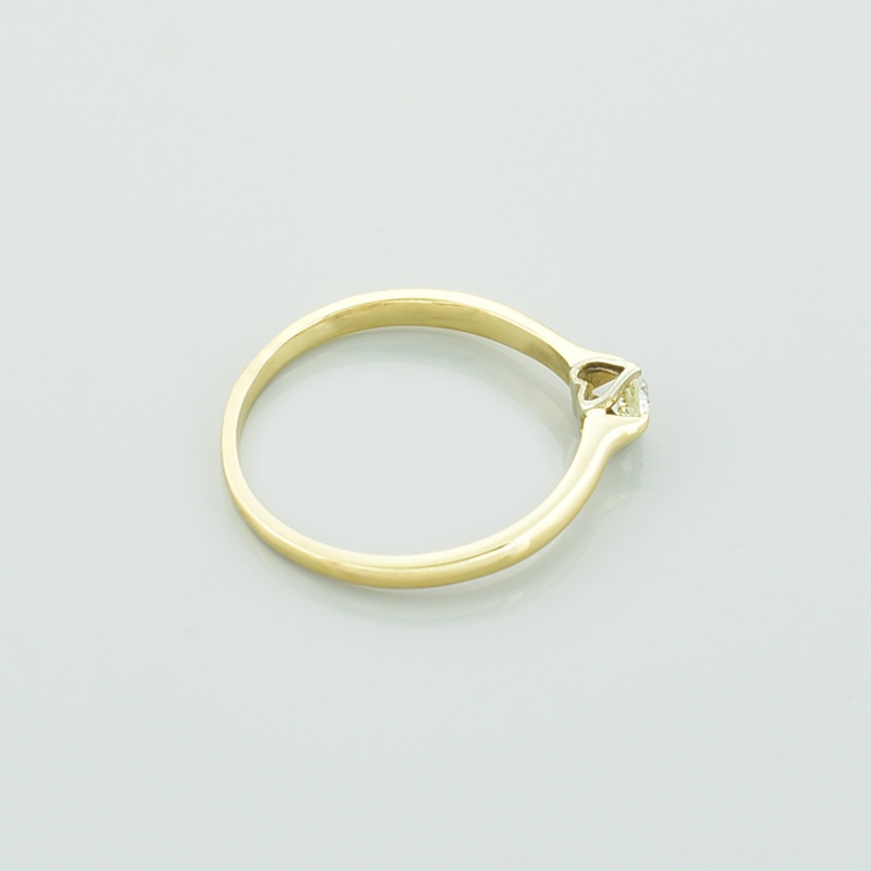Złoty pierścionek z brylantem serce leżący na prawym boku.