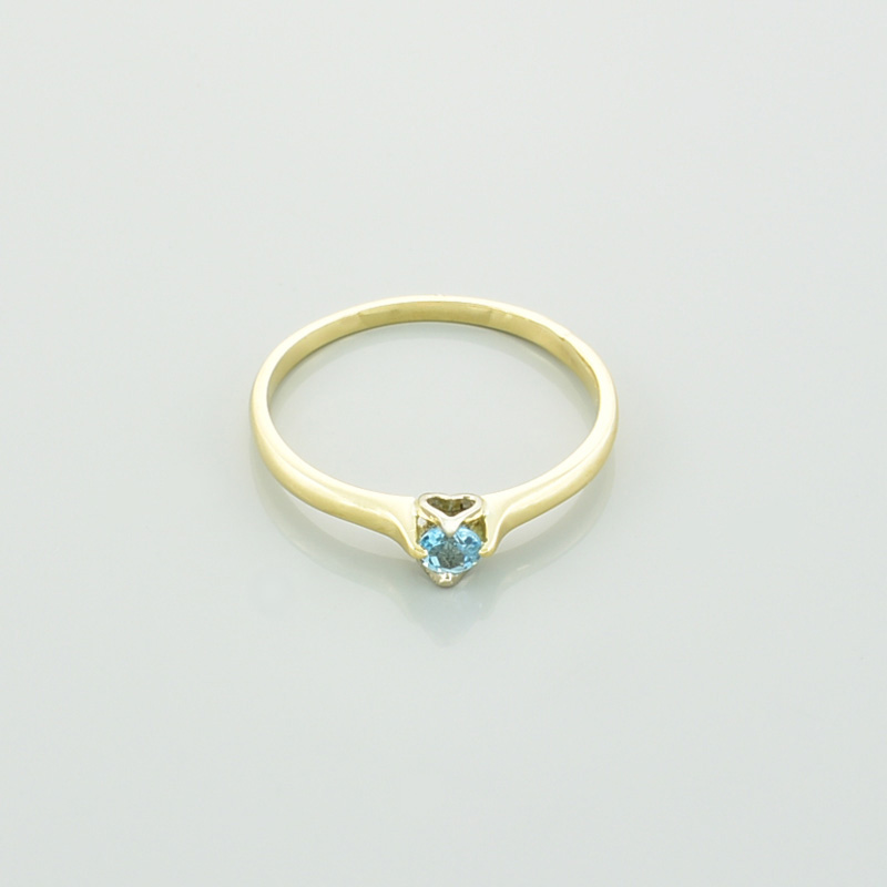 Złoty pierścionek serce z topazem w kolorze błękitnym leżący przodem.