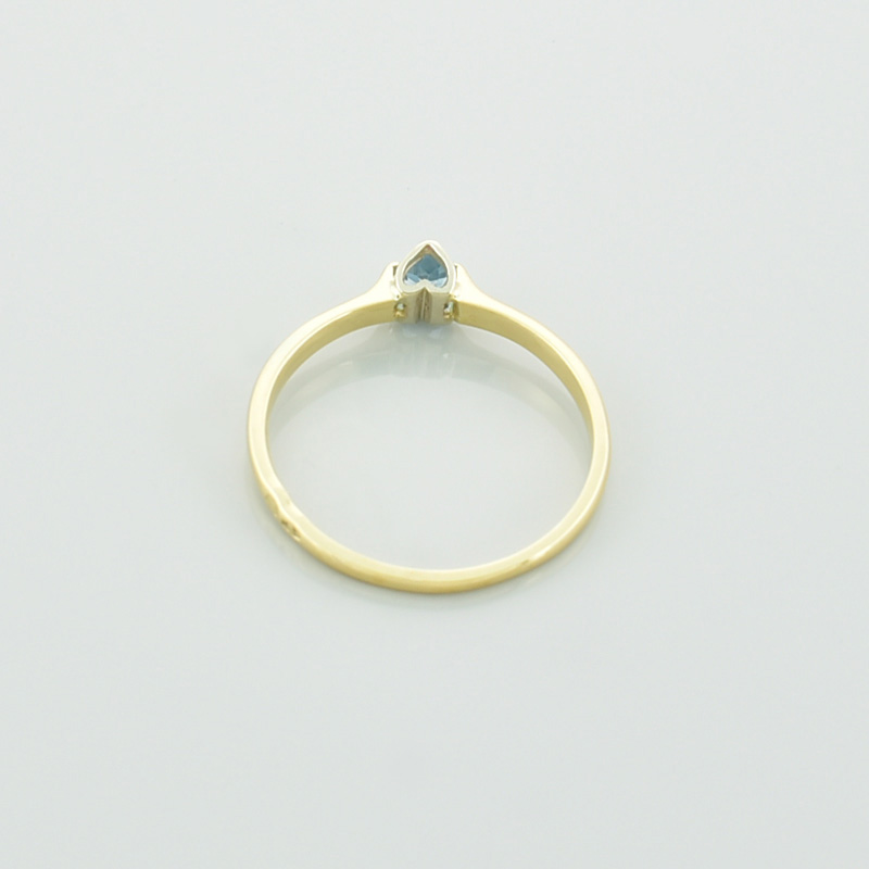 Złoty pierścionek serce z topazem w kolorze błękitnym leżący tyłem.