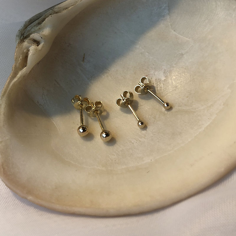 Złote kolczyki kulki 2 mm i kolczyki kulki 3 mm leżące na muszelce.