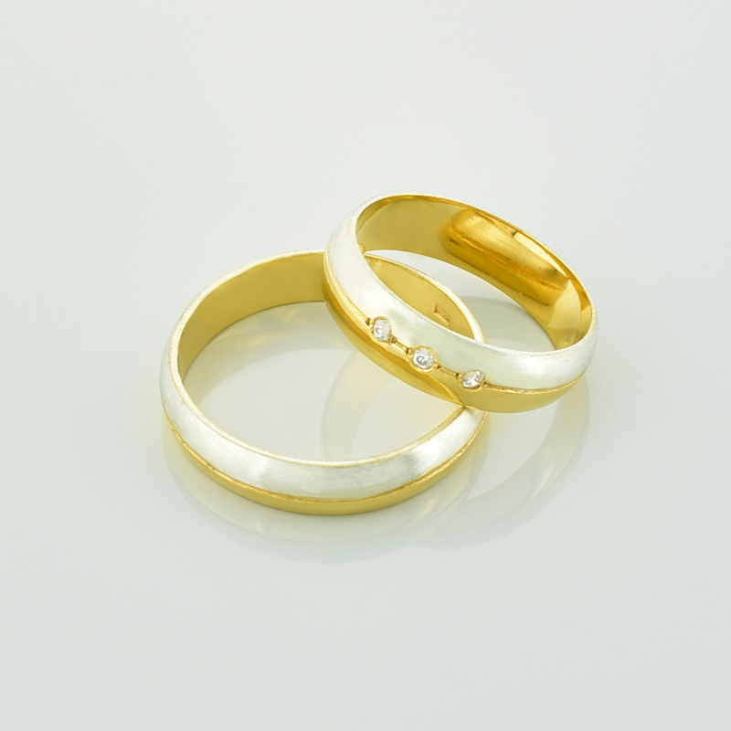Obrączki z brylantami dwukolorowe półokrągłe ze złota żółtego i białego leżące jedna na drugiej.