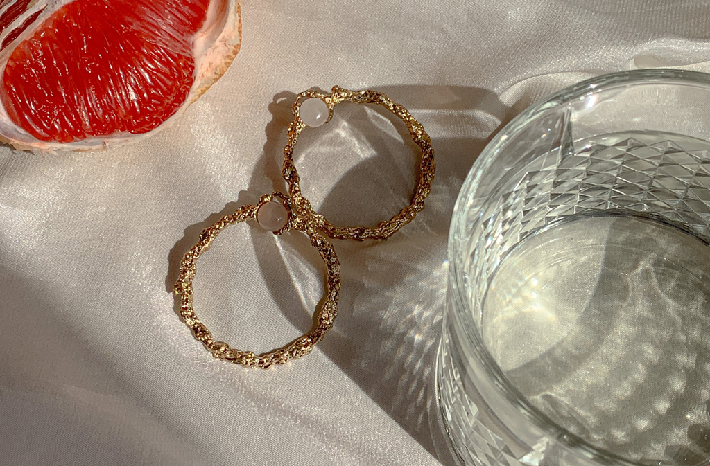 Kolczyki koła leżące na stole obok szklanki i kawałka grejpfruta.