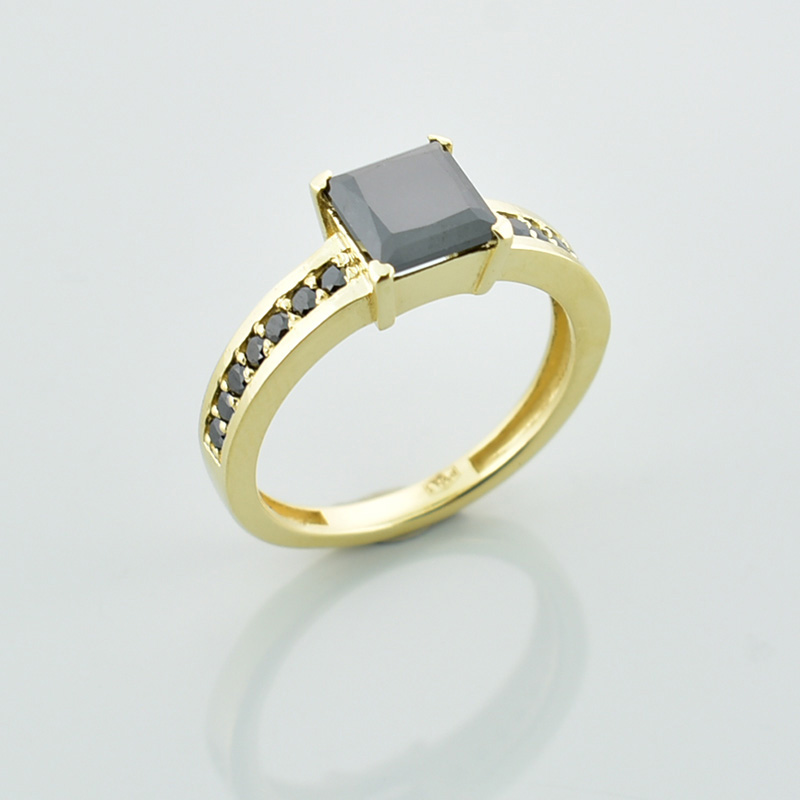 Złoty pierścionek z dużym, czarnym diamentem w formie kwadratu i wieloma małymi czarnymi diamentami po bokach.