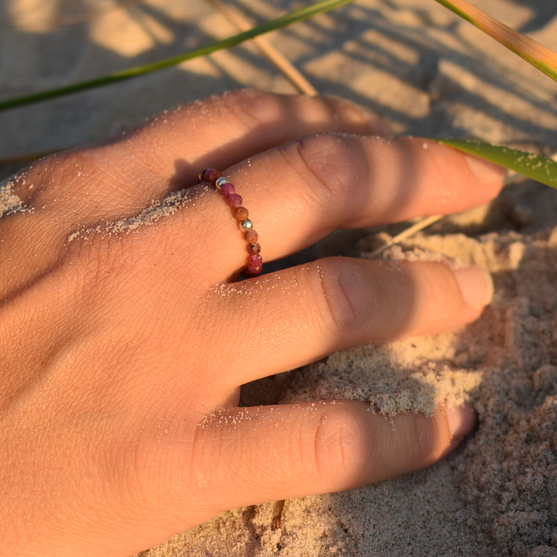 Pierścionek na gumce z okrągłych kamieni naturalnych - rubinów i srebra, przedstawiony na dłoni leżącej w piasku.