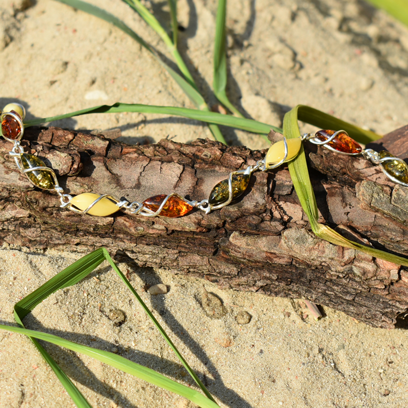 Srebrna bransoletka z bursztynami łezki przedstawiona na kawałku drewna na plaży.
