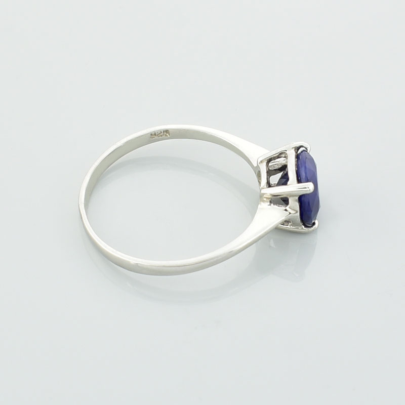 Srebrny subtelny pierścionek z szafirem o okrągłym kształcie, leżący na prawym boku.