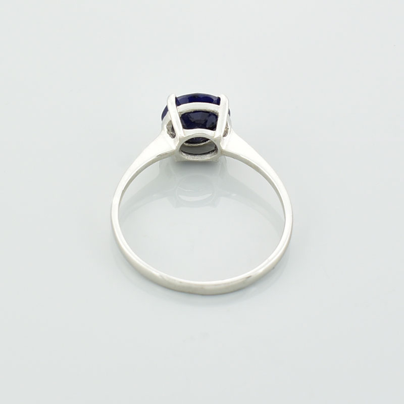 Srebrny subtelny pierścionek z szafirem o okrągłym kształcie leżący tyłem.