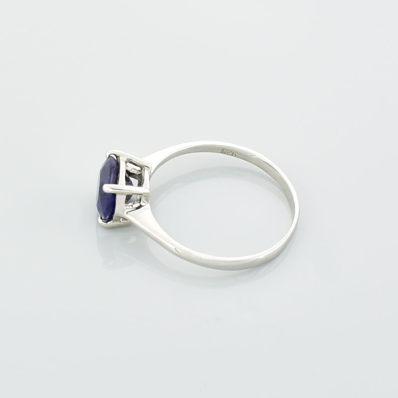 Srebrny subtelny pierścionek z szafirem o okrągłym kształcie leżący na lewym boku.