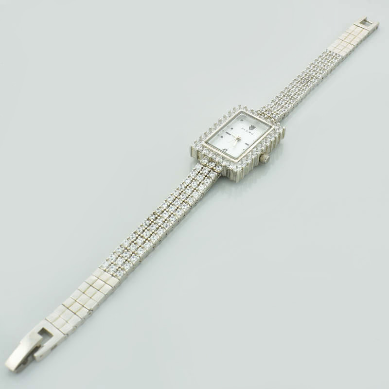 Srebrny zegarek damski z prostokątną tarczą, zdobiony małymi, białymi cyrkoniami.