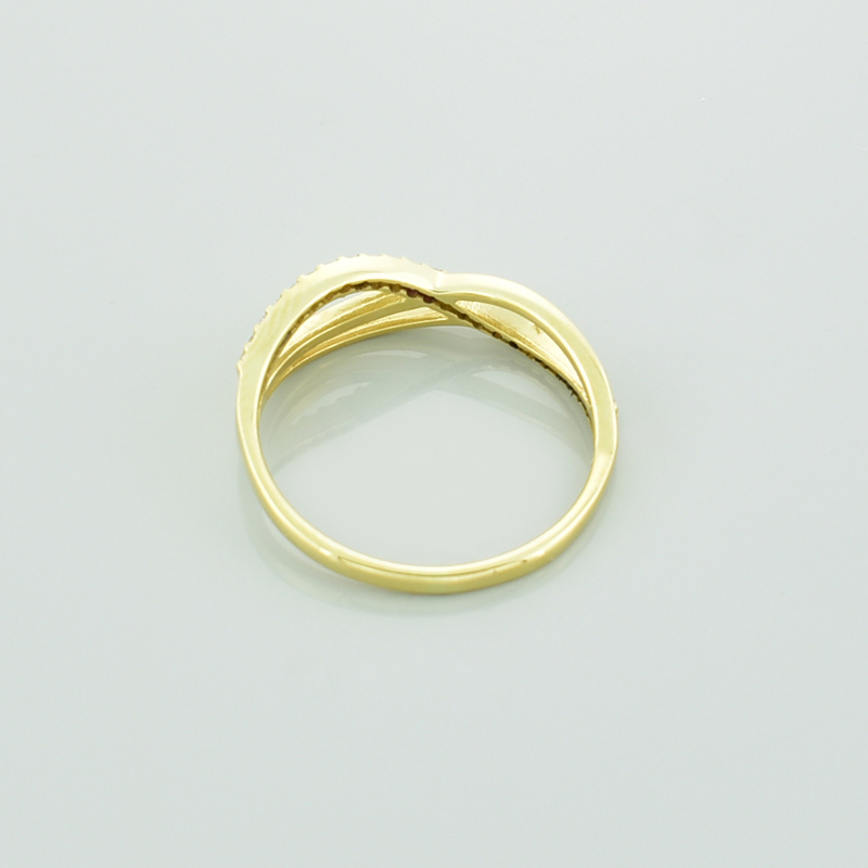 Złoty pierścionek z moissanitami i symbolem nieskończoności leżący tyłem.