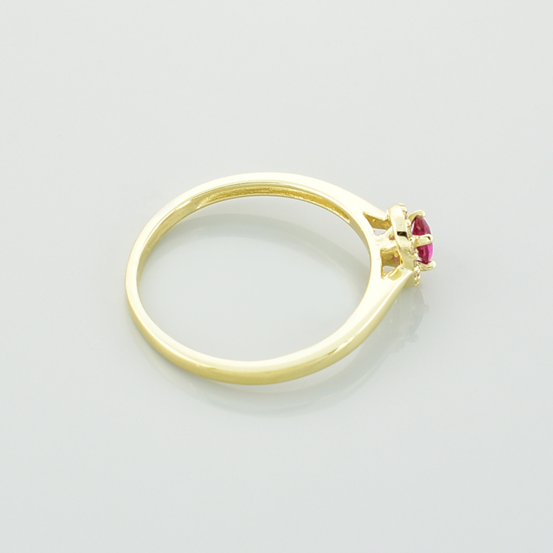 Złoty pierścionek z owalnym rubinem i białymi cyrkoniami pokazany bokiem.