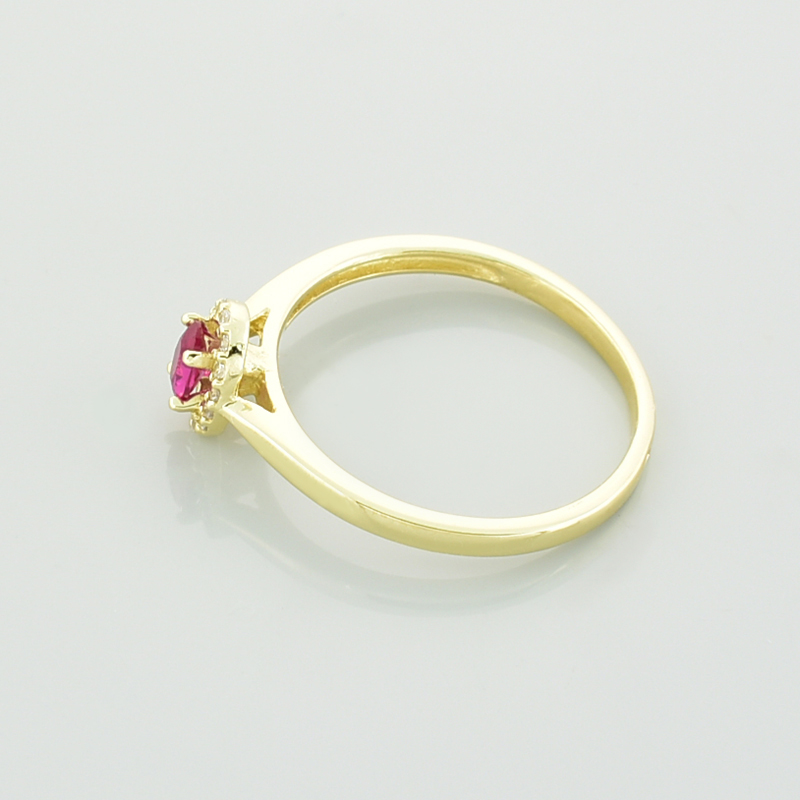 Złoty pierścionek z owalnym rubinem i białymi cyrkoniami leżący bokiem.