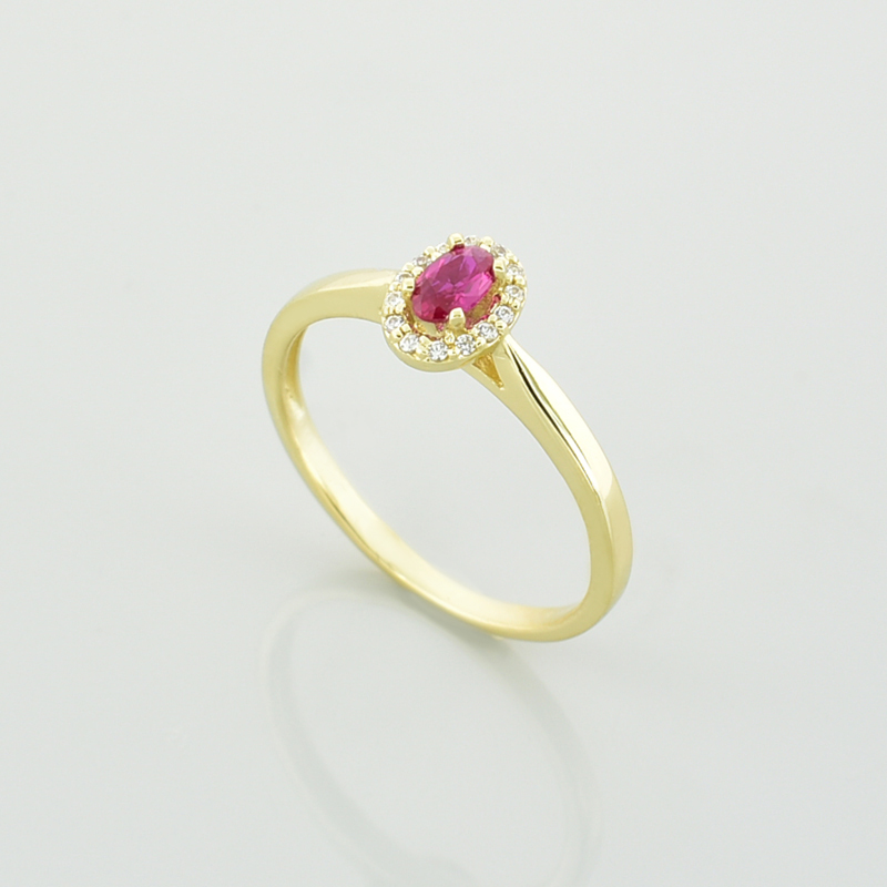 Złoty pierścionek z owalnym kamieniem o rubinowym kolorze i białymi cyrkoniami.