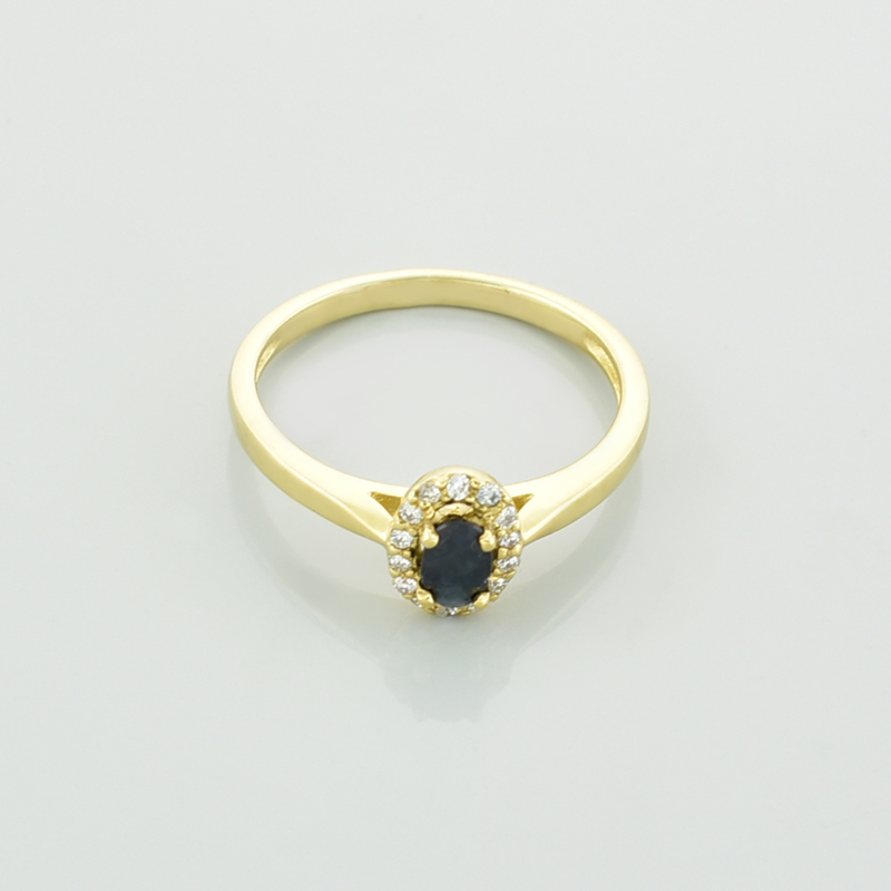 Złoty pierścionek z szafirem owalnym i brylantami leżący na wprost.