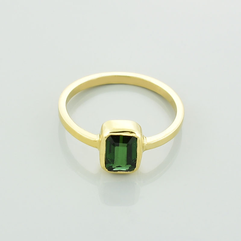 Złoty pierścionek z turmalinemw kolorze zielonym leżący przodem.