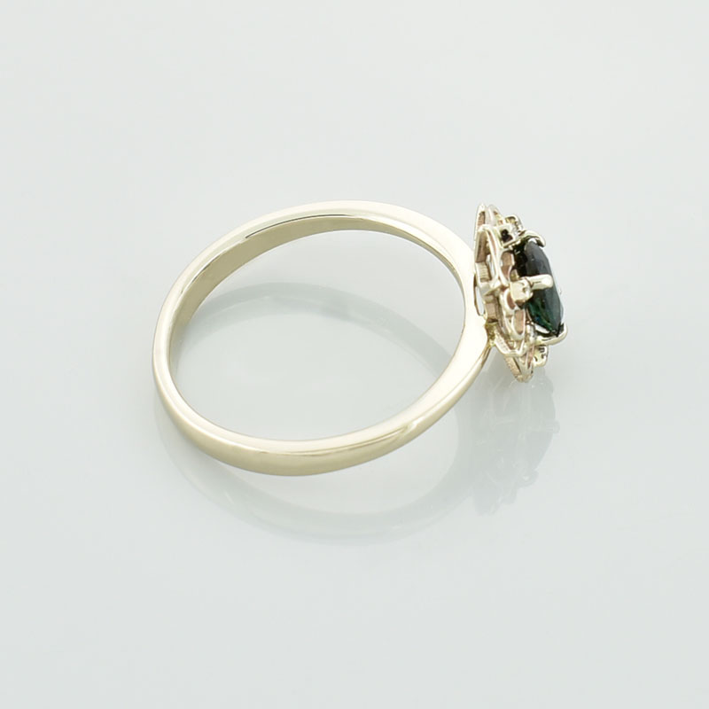 Złoty pierścionek z zielonym tanzanitem i brylantami w białym złocie 585 leżący bokiem.